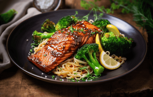 Plate of noodles topped with broccoli and bbq salmon garnished with lemon slices and sesame seeds