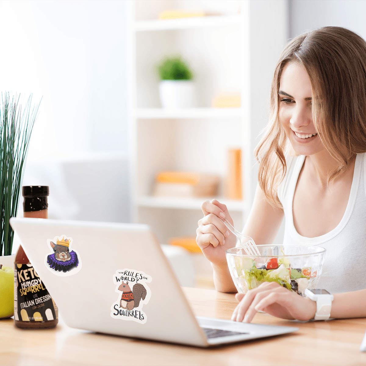 Young Lady enjoying a salad while on the laptop. The latop is decorated with the Hungry Squirrel Stickers